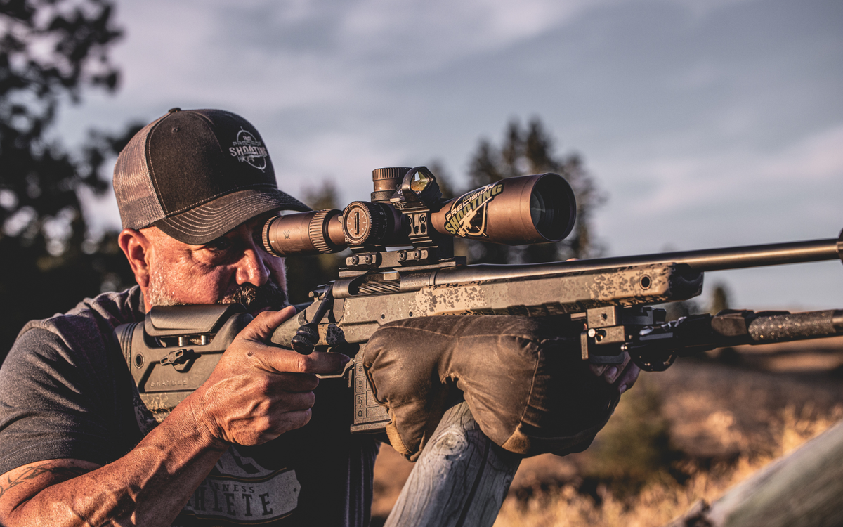Shooter aiming a rifle with a scope in a natural setting