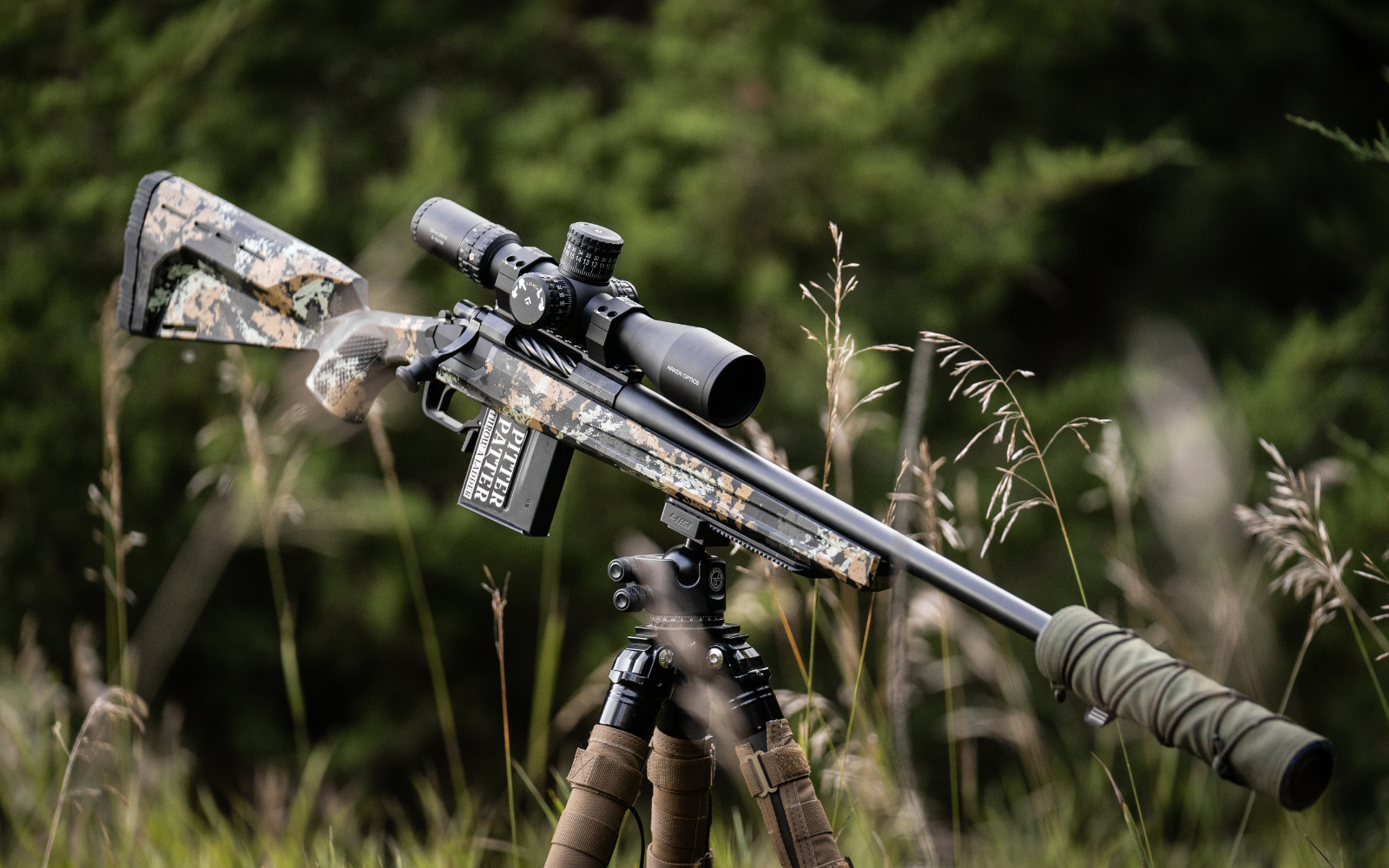 Camouflage rifle with scope on a tripod in a natural setting