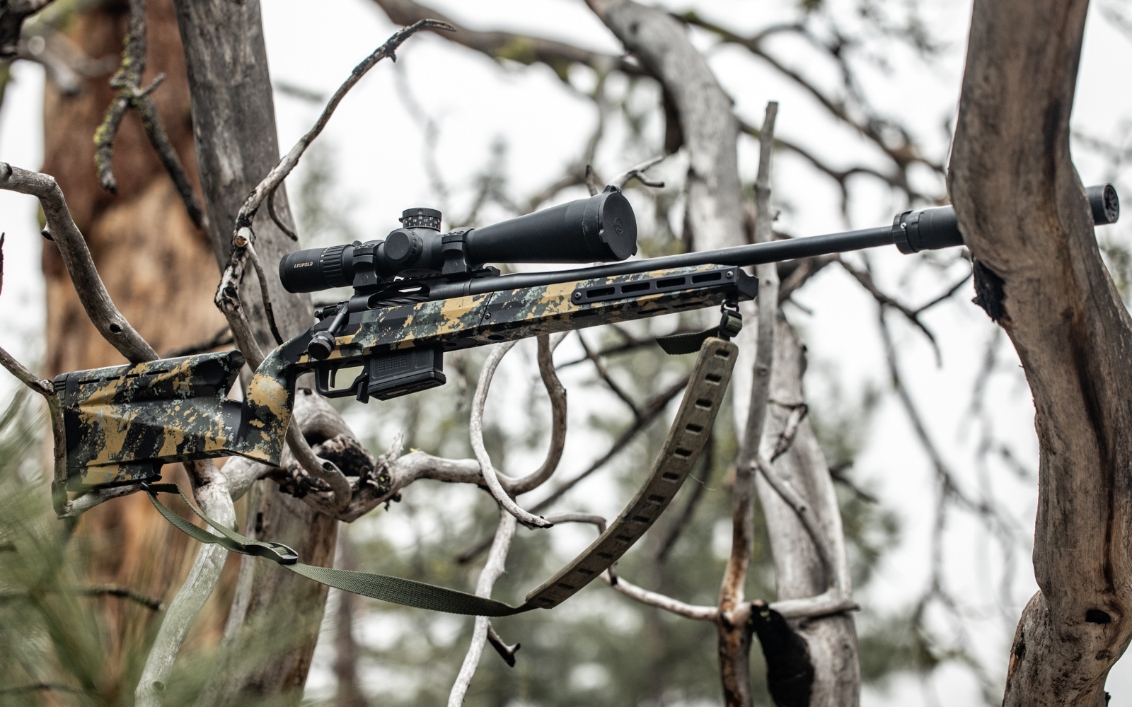 Hunter in camouflage gear with a rifle in a snowy forest