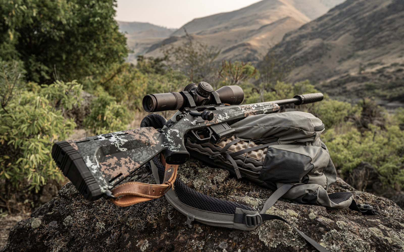 Camouflage rifle with scope on a tripod in a natural setting